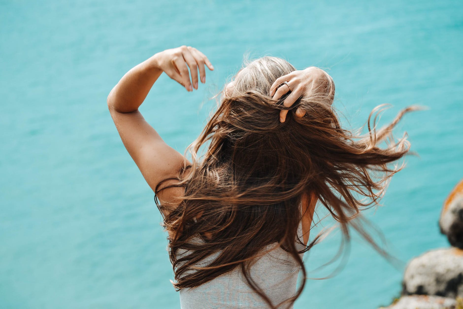 back view photo of woman in white sleeveless shirt running her fingers through her hair