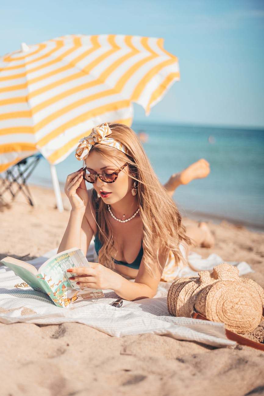 women s lying on the beach sand reading a book